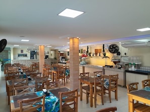 A restaurant with multiple tables and chairs, a kitchen area, and a bar. - Pousada Palmares (Cabo Frio)