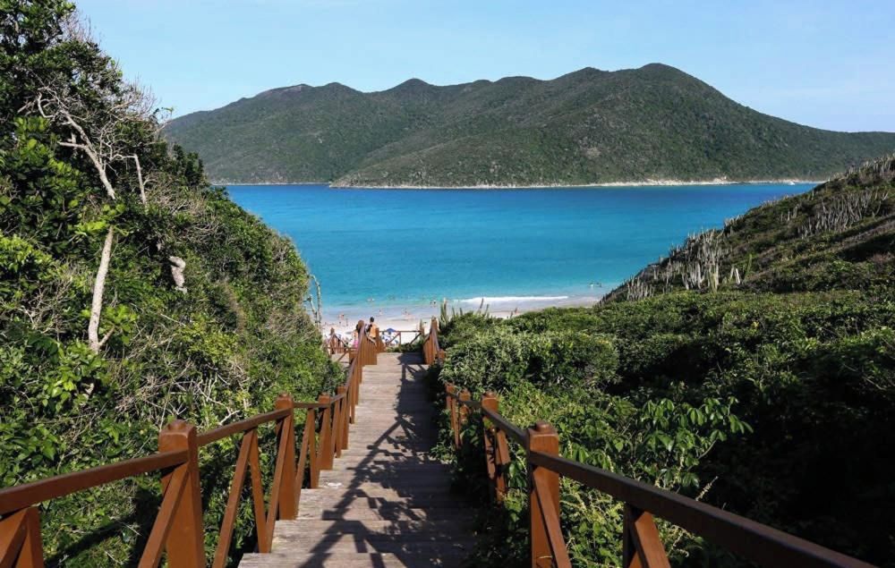 A wooden staircase leading to a beach with a clear view of the sea and mountains in the background.