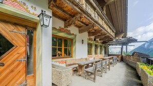 A traditional wooden building with a balcony, wooden benches, and a view of the mountains.