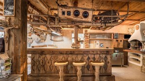 A rustic wooden bar area with a stone countertop, two stools, and a stone oven.