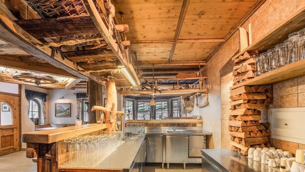 A rustic interior with a bar area, wooden beams, and a view of the outdoors.