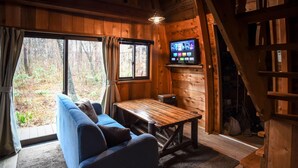 A cozy cabin interior with a sofa, a wooden table, and a television mounted on the wall. - The Hut (Hakuba)