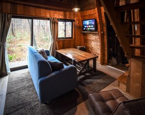 En mysig stuga med en soffa, ett träbord och en tv som är monterad på väggen.