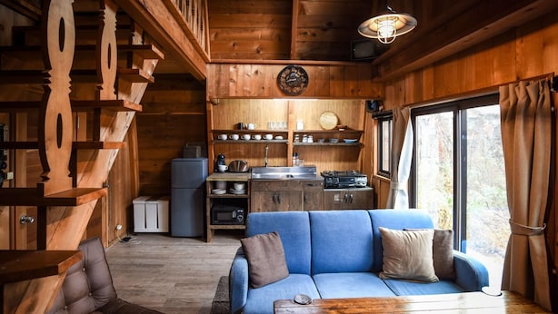 A compact cabin interior with a sofa, a dining table, a kitchenette, and a staircase. - The Hut (Hakuba)