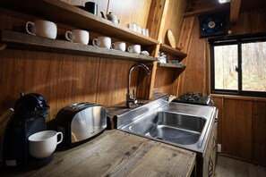 Een kleine keuken met houten wanden, een roestvrijstalen spoelbak, een gasfornuis en een koffiezetapparaat.