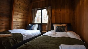 A cabin with two beds, wooden walls, and a window with curtains. - The Hut (Hakuba)