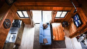 A cabin interior with a sofa, a television, a sink, and a window with curtains. - The Hut (Hakuba)