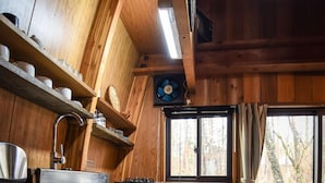 A wooden cabin interior with a kitchen area, including a sink, cabinets, and a window with curtains. - The Hut (Hakuba)