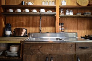 Una cocina con armarios de madera, un lavamanos de acero inoxidable y diferentes utensilios de cocina.
