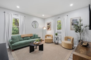 Un salon moderne avec un canapé vert, des fauteuils beiges, une table basse et un grand miroir rond accroché au mur.
