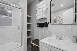 Une salle de bain avec une douche à parois de verre, un lavabo blanc, un miroir et un porte-serviettes avec des serviettes.