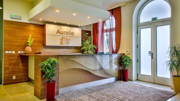 Una recepción con un cartel que dice 'Aurelie', una planta en maceta y una alfombra grande en el vestíbulo de un hotel.