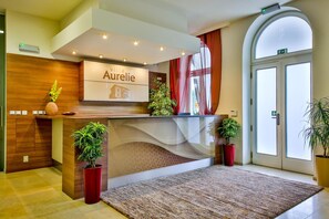 Una recepción con un cartel que dice 'Aurelie', una planta en maceta y una alfombra grande en el vestíbulo de un hotel.
