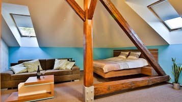Un dormitorio tipo loft con techo inclinado, estructura de cama de madera, sofá y una pequeña mesa.
