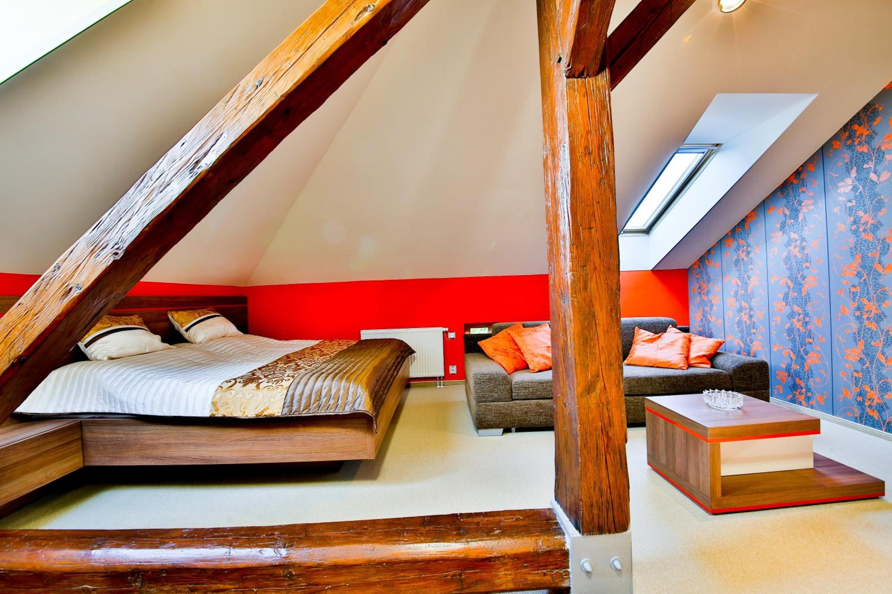 A bedroom with a sloped ceiling, a bed, a sofa, and a small table.