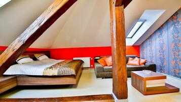 A bedroom with a sloped ceiling, a bed, a sofa, and a small table.