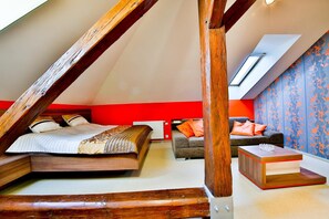 A bedroom with a sloped ceiling, a bed, a sofa, and a small table.