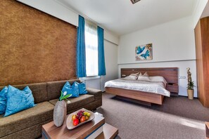 A hotel room with a bed, a sofa, a coffee table with fruit, a vase, and a painting on the wall.