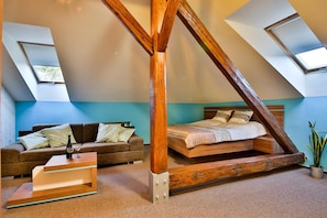 A loft bedroom with a sloped ceiling, a wooden bed frame, a sofa, and a small table. - Villa Aurelie (Velke Losiny)