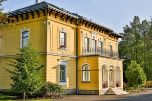 A yellow building with a balcony, large windows, and a stone foundation.