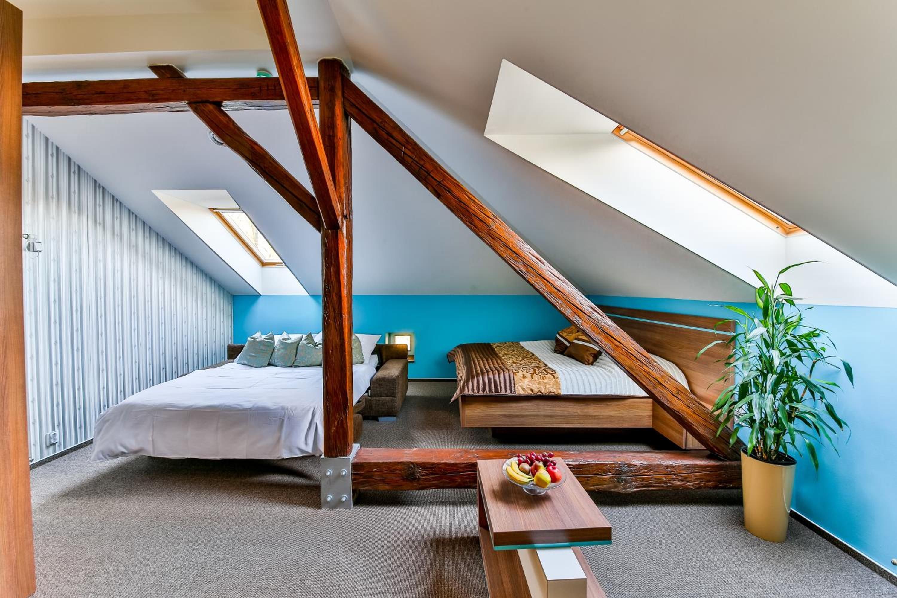 A bedroom with a sloped ceiling, a bed, a sofa, a small table with fruit, and a potted plant.