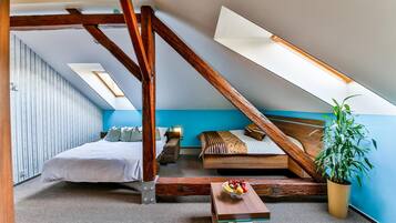 A bedroom with a sloped ceiling, a bed, a sofa, a small table with fruit, and a potted plant.