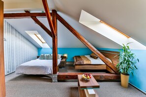 A bedroom with a sloped ceiling, a bed, a sofa, a small table with fruit, and a potted plant.