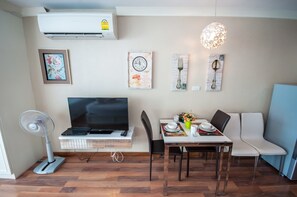 A modern living room with a flat-screen TV, a dining table with chairs, a wall-mounted air conditioner, and decorative wall art. - E205 Cozy 1-bedroom apartment pleasant with Kidclub near Beach (Nongkae)