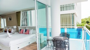 Quarto de hotel com cama, uma mesinha, duas cadeiras, varanda com vidro e piscina, e vista para área verde.
