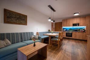 Una sala de estar moderna con un sofá, una mesa de comedor y sillas. Hay una zona de cocina con armarios de madera y un microondas.