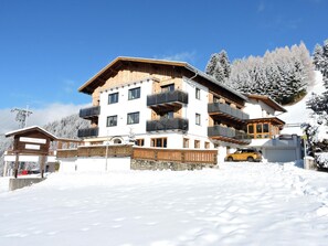 Un hotel de varios pisos con balcones, un telesilla al fondo y un paisaje cubierto de nieve.