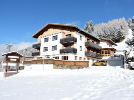 Un hotel de varios pisos con balcones, un telesilla al fondo y un paisaje cubierto de nieve.