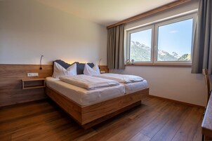 Un dormitorio con una cama de madera, una mesita de noche, una ventana con cortinas y vistas a las montañas.