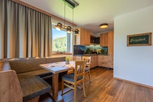 Una cocina moderna con armarios de madera, un comedor con banco y mesa, y vistas a un bosque por la ventana.