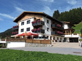 Un hotel de varios pisos con balcones, fachada de piedra y montañas al fondo.