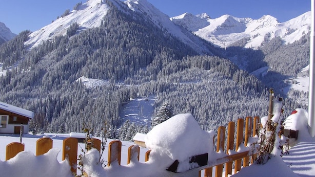 Un paisaje montañoso con laderas nevadas y un edificio con techo inclinado.