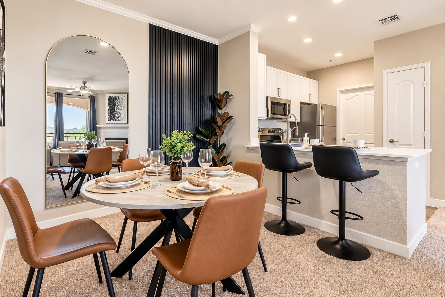 A dining area with a round table, brown chairs, and a kitchen in the background.