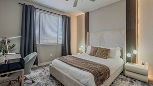 Habitación de hotel con cama, escritorio, silla y ventilador de techo.