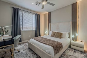 Quarto de hotel com cama, escrivaninha, cadeira e ventoinha de teto.