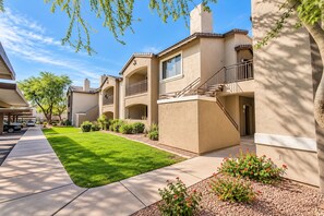 A residential building with a covered parking area, a well-maintained lawn, and a clear sky.