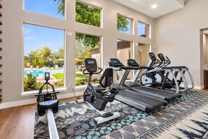Un gimnasio en casa con cintas de correr, una bicicleta estática y una máquina de remo, con vistas a una piscina.