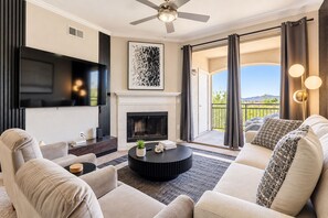 A modern living room with a flat-screen TV, fireplace, and a balcony with a view.