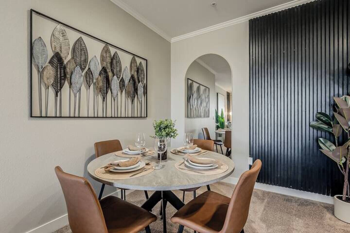 Un coin repas avec une table ronde dressée pour quatre personnes, entourée de chaises. Un grand tableau abstrait est accroché au mur, au-dessus de la table.