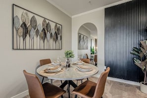 Een eetruimte met een ronde tafel voor vier personen, omringd door stoelen. Daarboven hangt een groot abstract schilderij aan de muur.