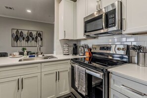 Cozinha moderna com eletrodomésticos de aço inoxidável, armários brancos e um detalhe decorativo na parede.