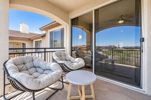 A balcony with two cushioned chairs and a small table, a sliding glass door, and a view of a cityscape.