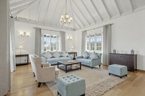 A spacious living room with a high ceiling, a chandelier, a sofa set, a coffee table, a side table, a lamp, a cabinet, and a window with curtains. - Aadya Tea Bangalows By Aahaasa (Upcot)