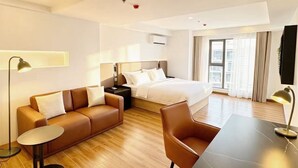 A modern hotel room with a bed, a sofa, a dining table, and a desk.