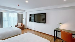 A hotel room with two beds, a desk, a chair, a TV, and a window with curtains.