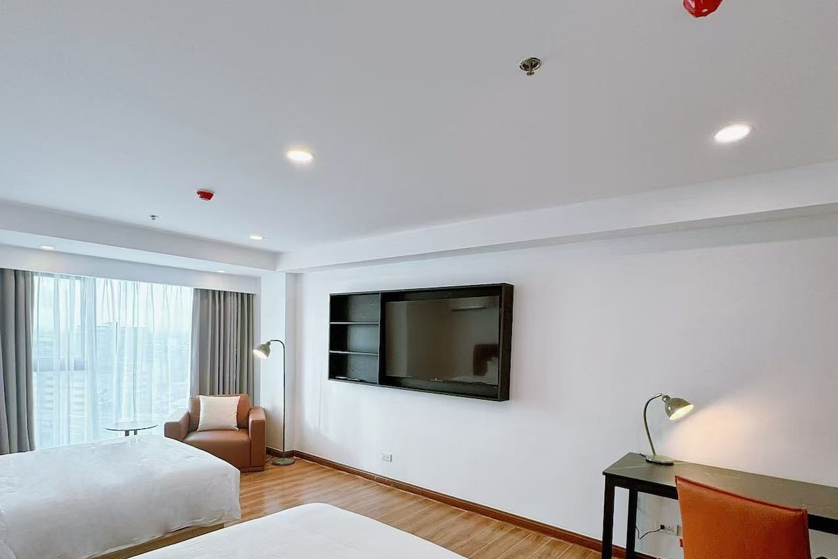 Habitación de hotel con dos camas, un escritorio, una silla, un televisor y una ventana con cortinas.